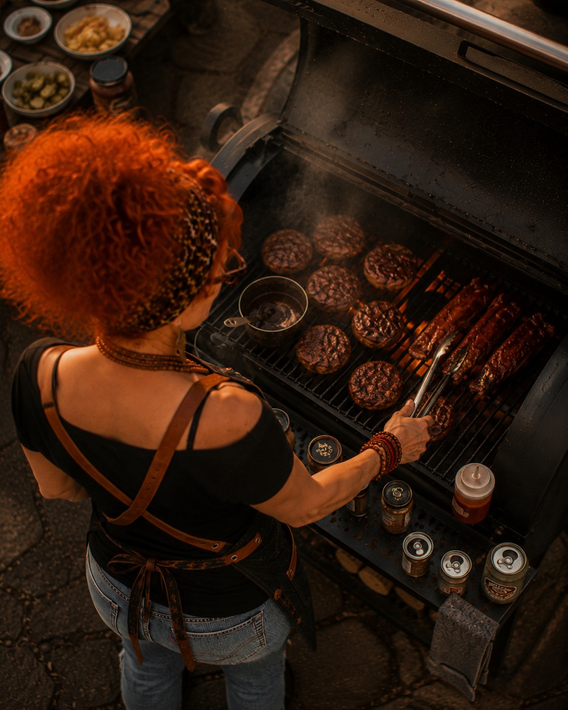 An overhead view of Winnie working the grill, burgers and ribs sizzling alongside a small saucepan
